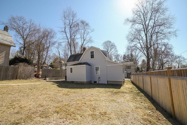 rear view of house featuring a gambrel roof, roof with shingles, a chimney, a fenced backyard, and a yard