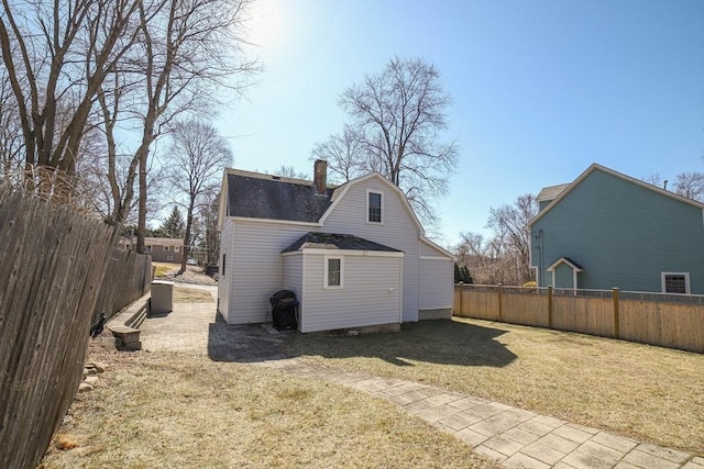 back of house with a gambrel roof, roof with shingles, a lawn, a chimney, and a fenced backyard