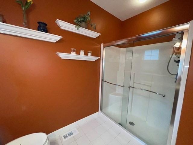 bathroom featuring tile patterned flooring, a shower with shower door, and toilet