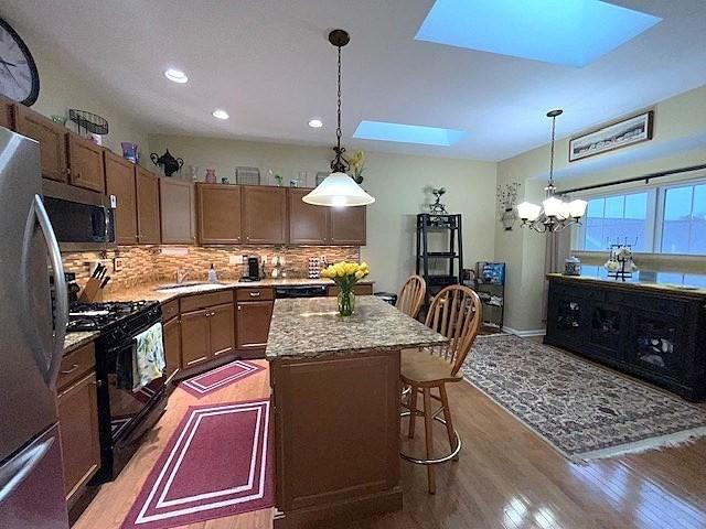 kitchen with light hardwood / wood-style flooring, a skylight, decorative light fixtures, a kitchen island, and stainless steel appliances