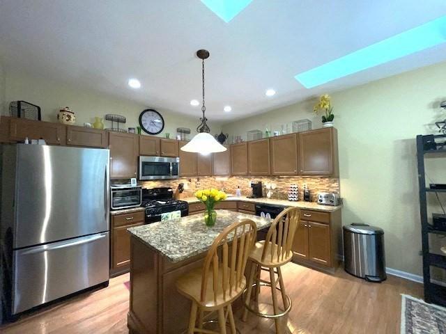 kitchen with a center island, hanging light fixtures, a skylight, light wood-type flooring, and appliances with stainless steel finishes