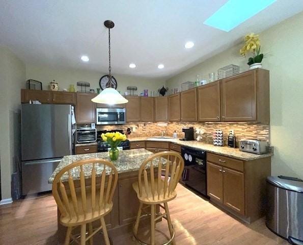 kitchen featuring appliances with stainless steel finishes, a skylight, pendant lighting, light hardwood / wood-style flooring, and a center island