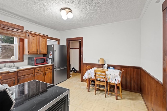 12 Leonard St, Somerville, MA 02144 - kitchen featuring stainless steel appliances, a wainscoted wall, brown cabinetry, light flooring, and wood walls