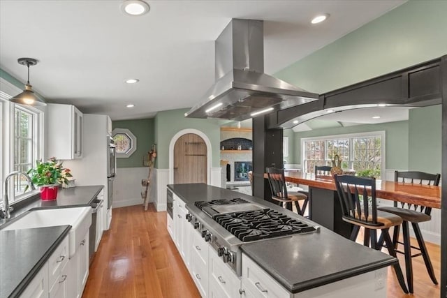 279 Norfolk St, Holliston, MA 01746 - kitchen featuring island exhaust hood, dark countertops, stainless steel gas stovetop, white cabinets, and wainscoting