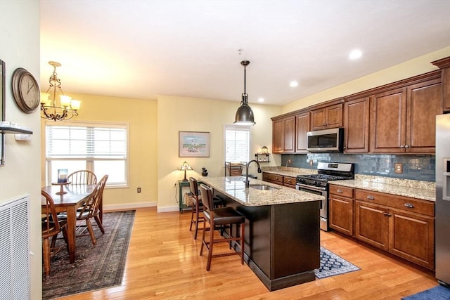 kitchen featuring stainless steel appliances, decorative backsplash, light wood-style floors, a healthy amount of sunlight, and a sink