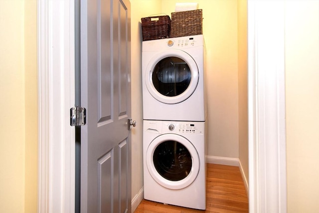 laundry room featuring baseboards, laundry area, stacked washer / dryer, and light wood-style floors