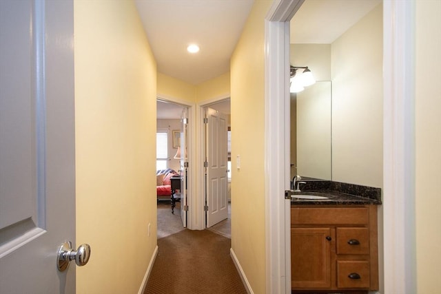 hallway featuring baseboards, dark colored carpet, and a sink