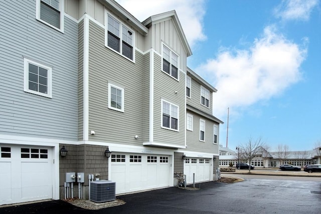 view of side of property featuring board and batten siding, cooling unit, driveway, and a garage