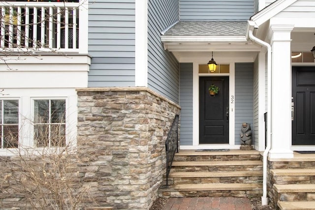 entrance to property with stone siding and roof with shingles