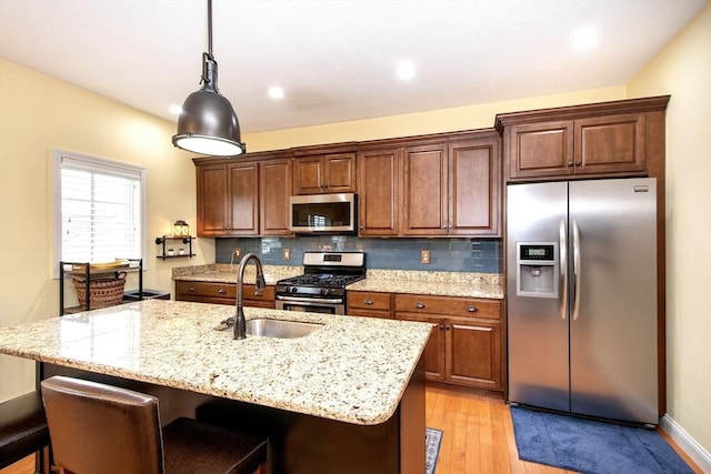 kitchen featuring stainless steel appliances, a sink, decorative backsplash, a kitchen bar, and a center island with sink