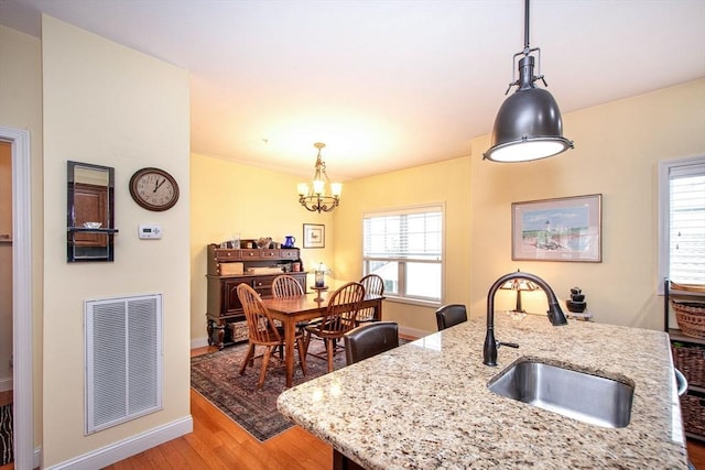 kitchen featuring visible vents, light wood-style flooring, hanging light fixtures, an inviting chandelier, and a sink