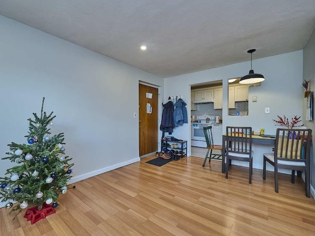 interior space featuring light wood-type flooring, backsplash, a textured ceiling, decorative light fixtures, and white electric stove