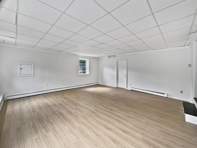 empty room featuring a paneled ceiling, baseboard heating, and light hardwood / wood-style flooring