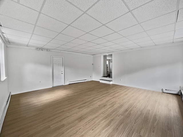 empty room with a baseboard heating unit, wood-type flooring, and a paneled ceiling