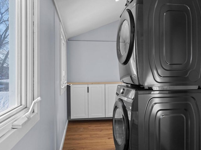 laundry room featuring a healthy amount of sunlight, cabinets, stacked washer / dryer, and light hardwood / wood-style floors