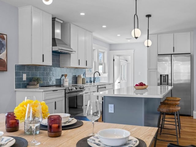 kitchen featuring appliances with stainless steel finishes, white cabinetry, wall chimney exhaust hood, and decorative light fixtures