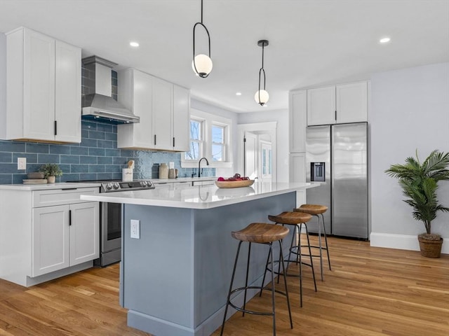 kitchen with white cabinetry, pendant lighting, a kitchen island, wall chimney range hood, and stainless steel appliances