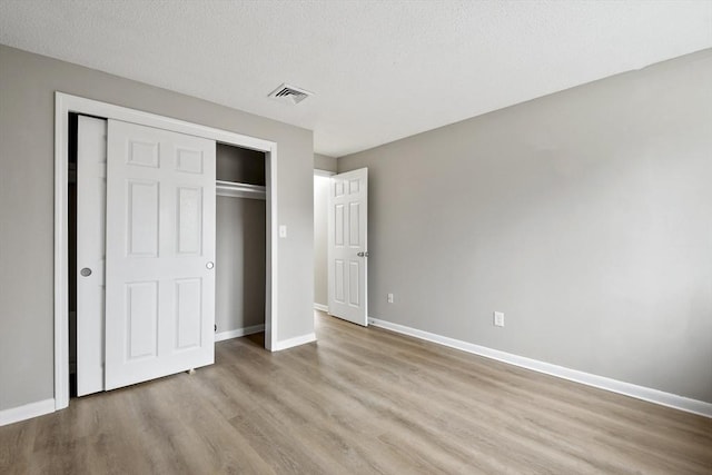 unfurnished bedroom with a closet, a textured ceiling, visible vents, light wood finished floors, and baseboards