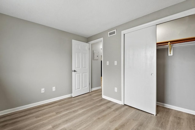 unfurnished bedroom featuring wood finished floors, a closet, baseboards, and visible vents