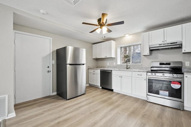 kitchen with a sink, a ceiling fan, light wood finished floors, appliances with stainless steel finishes, and under cabinet range hood