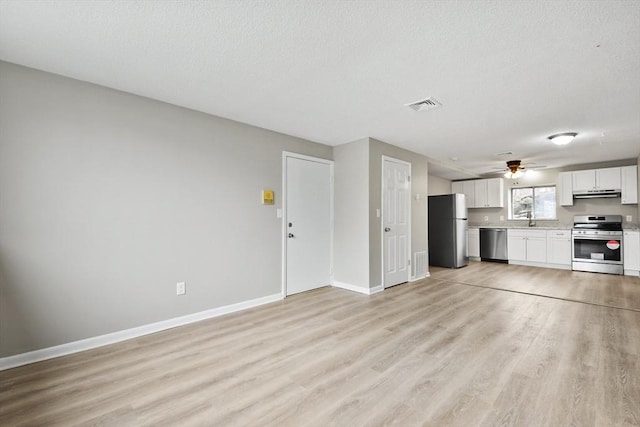 unfurnished living room with a sink, a textured ceiling, baseboards, visible vents, and light wood-style floors