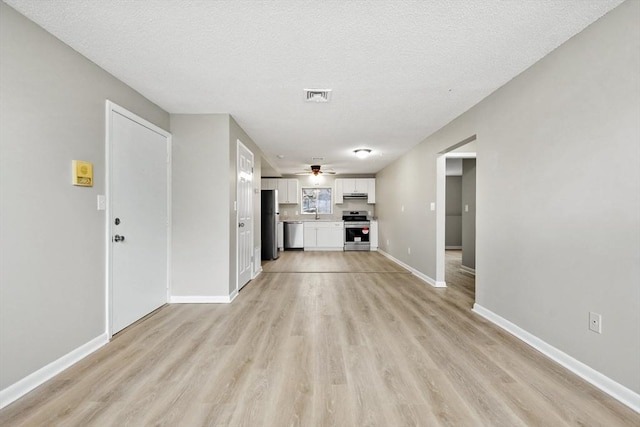 unfurnished living room featuring a textured ceiling, light wood-style flooring, baseboards, visible vents, and ceiling fan