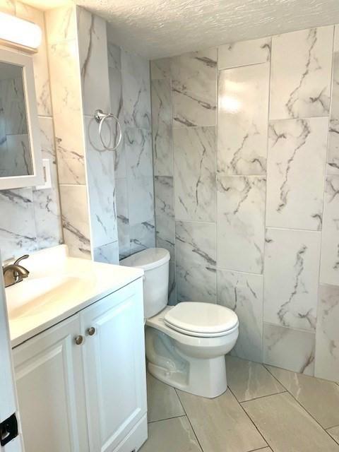 bathroom featuring a textured ceiling, toilet, vanity, and tile walls