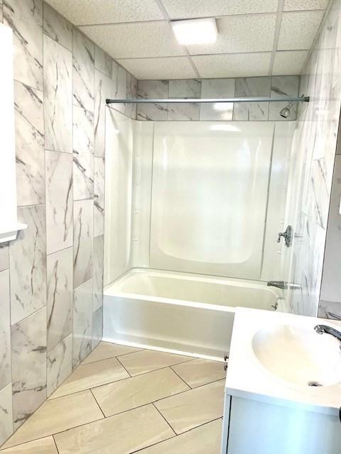 bathroom featuring vanity, washtub / shower combination, and a drop ceiling