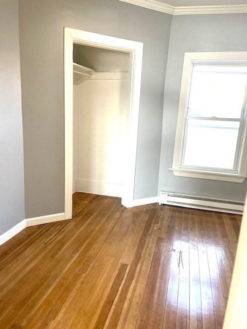 unfurnished bedroom with a closet, crown molding, baseboard heating, and wood-type flooring