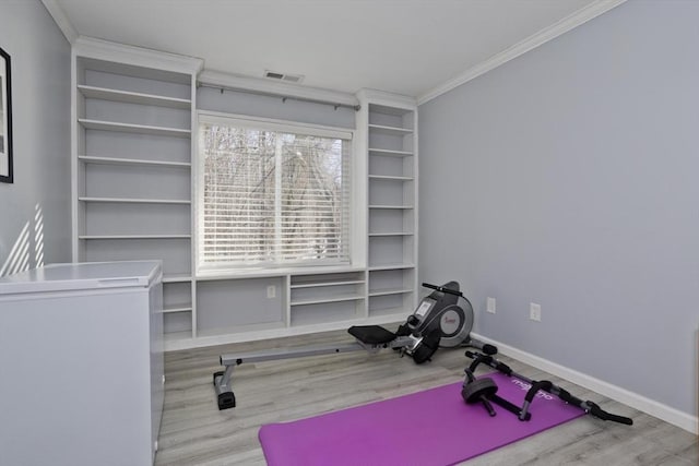 exercise room with ornamental molding, light wood-type flooring, visible vents, and baseboards