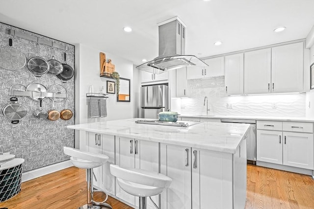 kitchen featuring light wood finished floors, a kitchen island, appliances with stainless steel finishes, island exhaust hood, and white cabinets