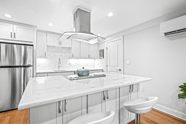 kitchen featuring cooktop, a wall unit AC, island exhaust hood, freestanding refrigerator, and a sink