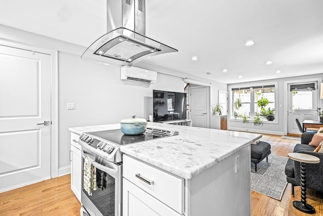 kitchen featuring a wall unit AC, light stone counters, a kitchen island, stainless steel electric stove, and island range hood