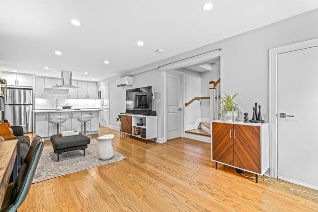 living room with stairs, an AC wall unit, recessed lighting, and light wood finished floors