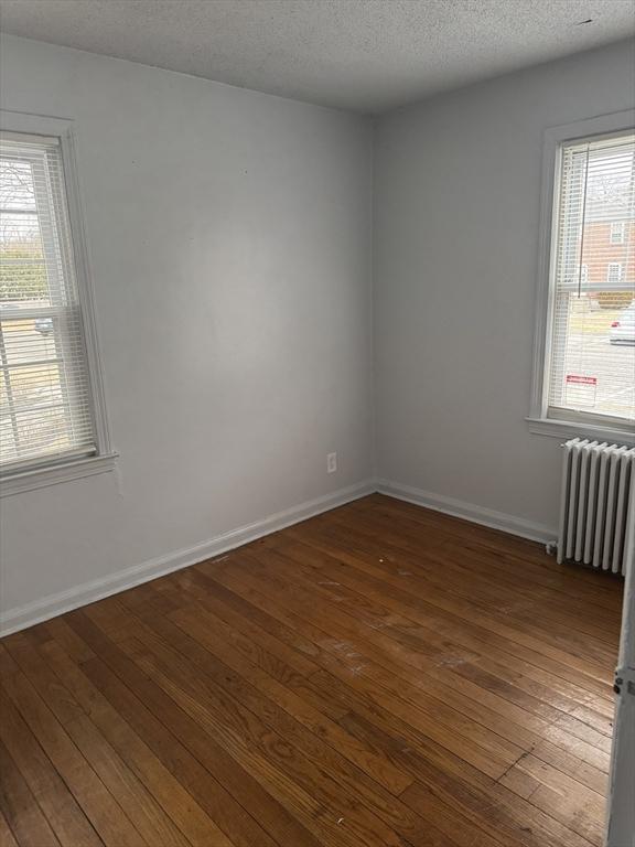 unfurnished room with a healthy amount of sunlight, dark hardwood / wood-style floors, radiator, and a textured ceiling