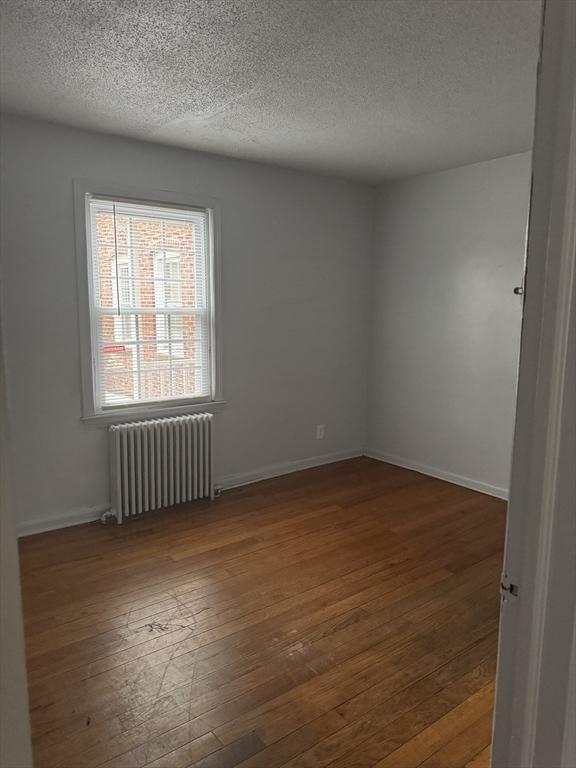 spare room with dark hardwood / wood-style flooring, radiator, and a textured ceiling