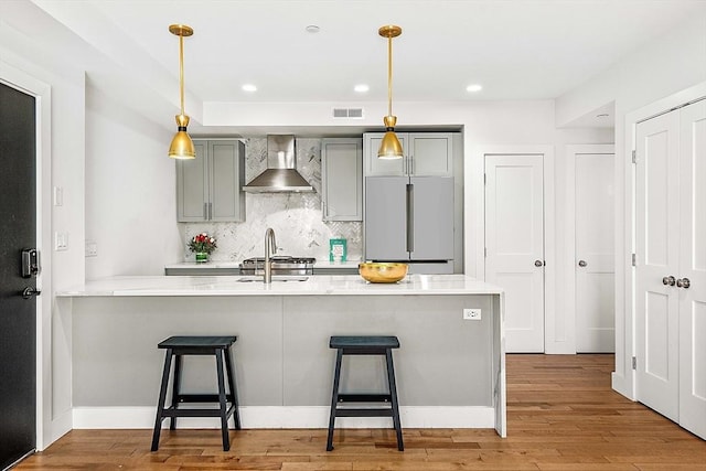 kitchen featuring built in refrigerator, wall chimney exhaust hood, a kitchen bar, tasteful backsplash, and gray cabinetry