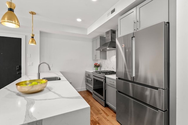 kitchen featuring decorative backsplash, hanging light fixtures, light stone countertops, stainless steel appliances, and wall chimney exhaust hood