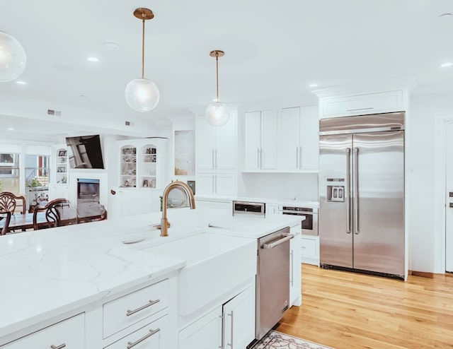 kitchen featuring stainless steel appliances, pendant lighting, light wood-type flooring, white cabinetry, and light stone counters