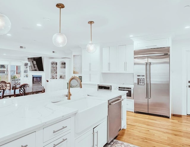 56 Belmont St Unit 3, Boston, MA 02129 - kitchen with stainless steel appliances, decorative light fixtures, white cabinets, light wood-style floors, and a glass covered fireplace