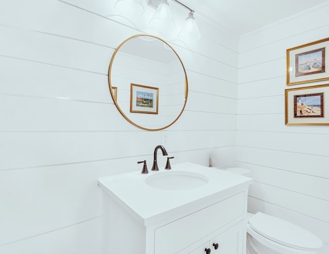 bathroom with vanity, toilet, and wood walls