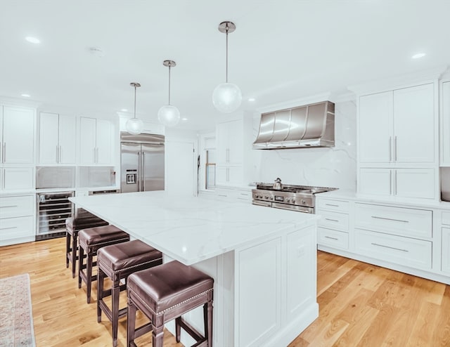 kitchen featuring premium appliances, light hardwood / wood-style floors, wall chimney exhaust hood, pendant lighting, and beverage cooler