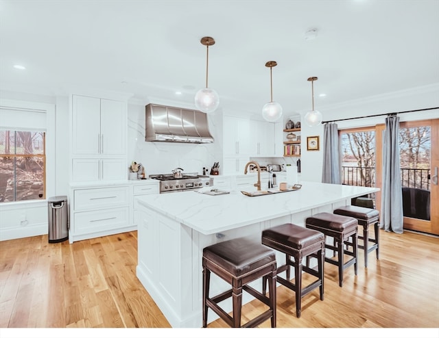 kitchen featuring wall chimney exhaust hood, white cabinets, light hardwood / wood-style floors, and a center island with sink