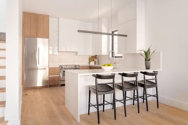 kitchen featuring appliances with stainless steel finishes, backsplash, light hardwood / wood-style floors, white cabinetry, and a breakfast bar area