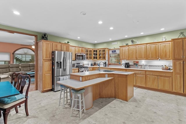 kitchen with stainless steel appliances, sink, a kitchen bar, ceiling fan, and a center island with sink