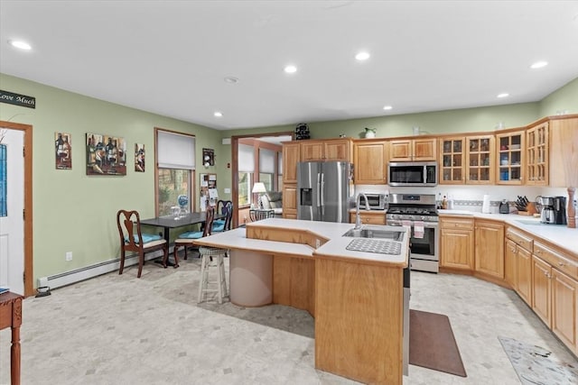 kitchen featuring sink, a center island with sink, baseboard heating, a breakfast bar, and appliances with stainless steel finishes