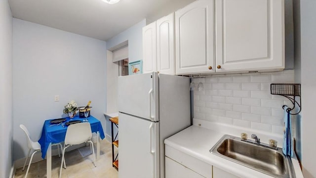 kitchen featuring a sink, decorative backsplash, white cabinetry, and freestanding refrigerator