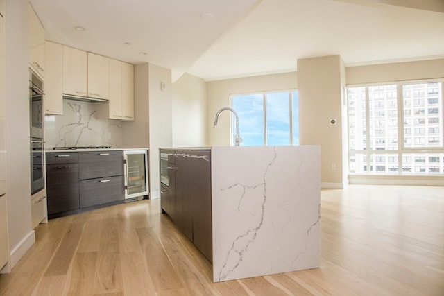 kitchen with white cabinets, decorative backsplash, beverage cooler, and light hardwood / wood-style flooring