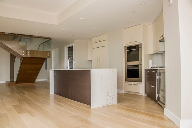 kitchen featuring white cabinets, light wood-type flooring, double oven, and beverage cooler