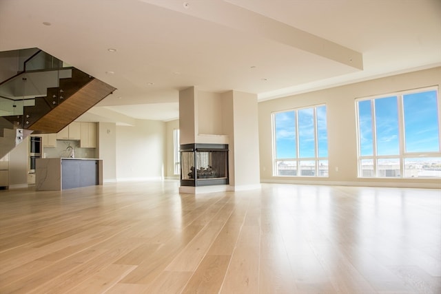 unfurnished living room featuring a multi sided fireplace and light hardwood / wood-style floors